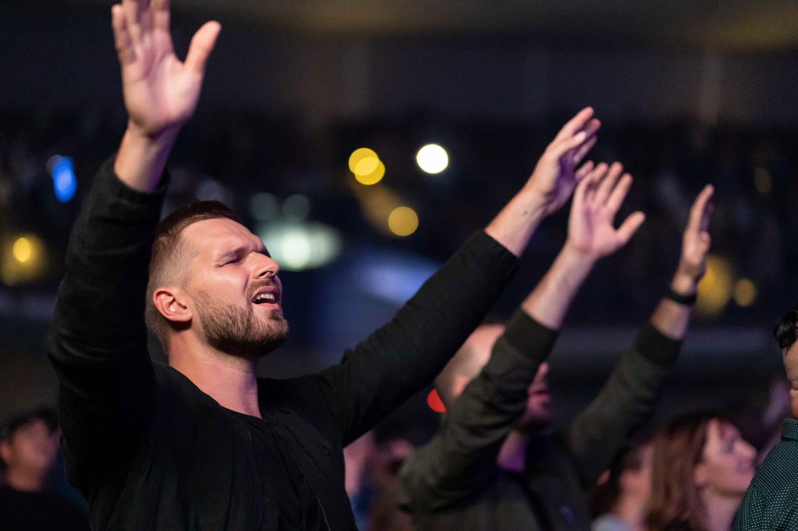 Man with hands up and eyes closed in a crowd